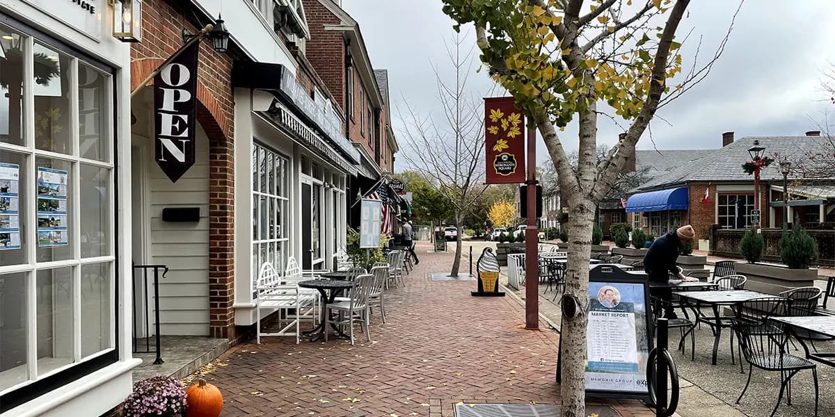 A brick-paved street lined with shops and outdoor seating, featuring an "OPEN" sign and autumn foliage.