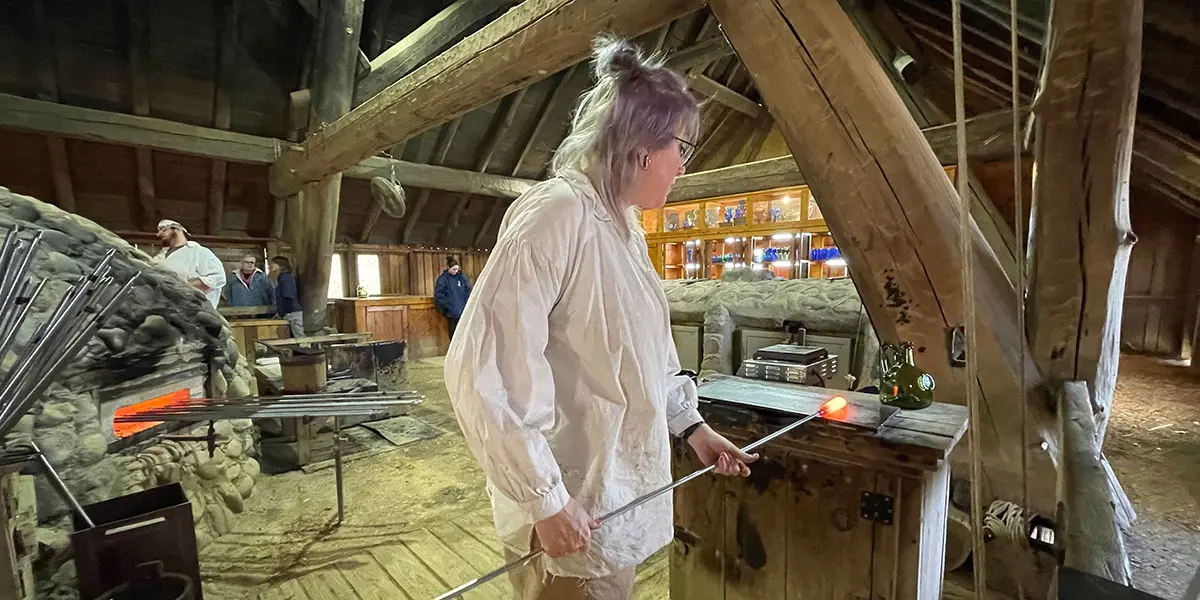 A glassblower shapes molten glass in a rustic workshop.