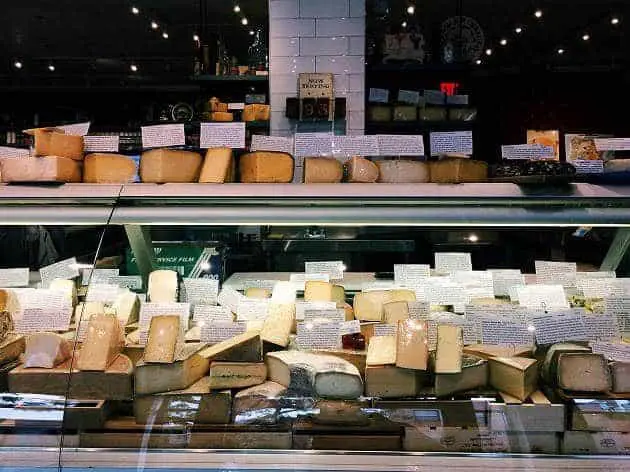 A display case filled with various types of cheese, each labeled with descriptive tags.