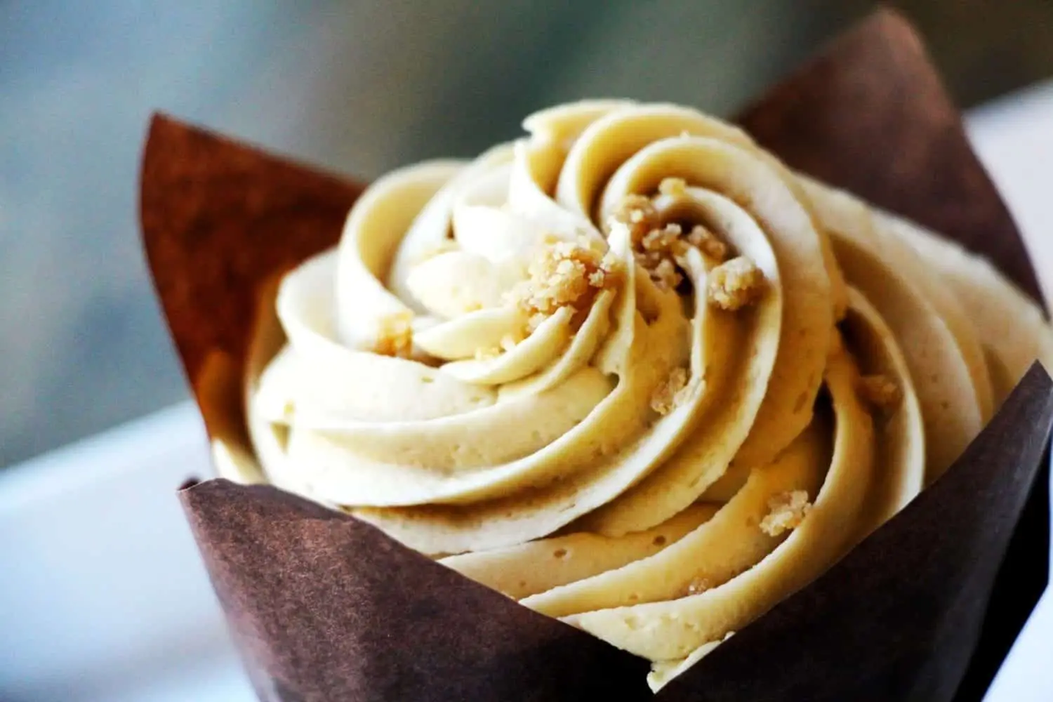 Close-up of a frosted cupcake with a swirl of creamy icing and crumbs on top.