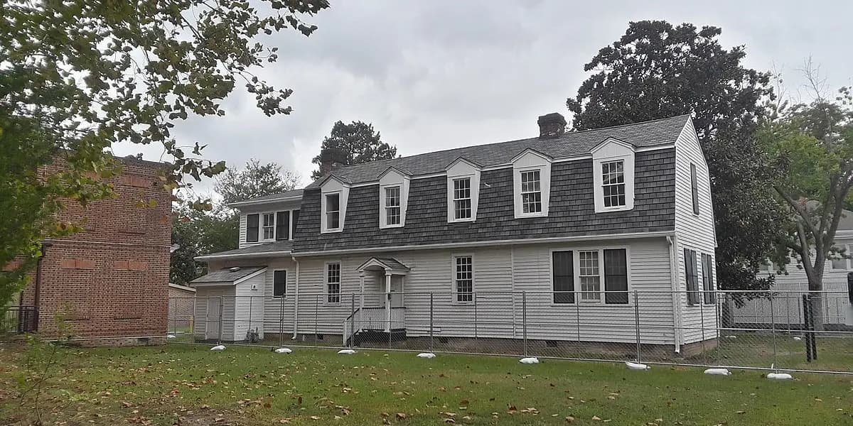 A two-story house with a gray shingle roof and white siding, surrounded by a lawn and trees.