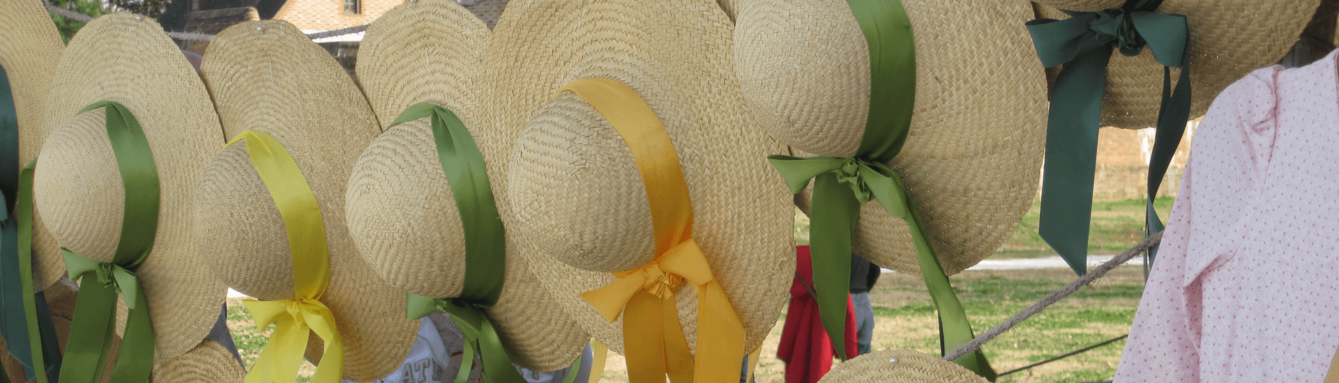 A row of straw wide brimmed hats with multi color ribbons
