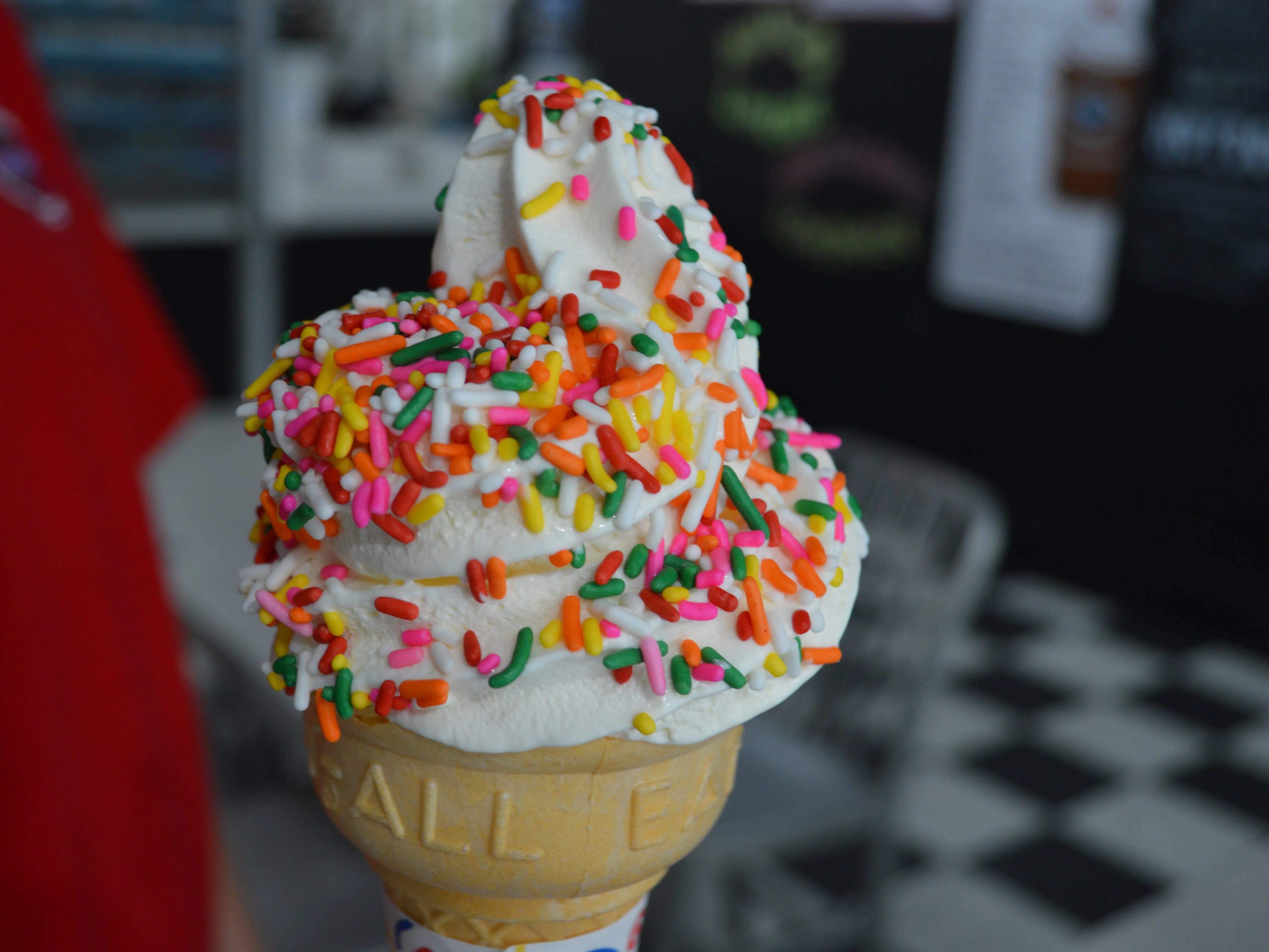 A close-up of a cone topped with swirled soft serve ice cream and colorful sprinkles.