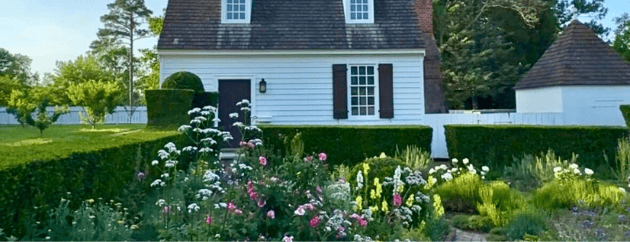 A charming white house with a sloped roof and surrounded by a lush garden filled with colorful flowers and neatly trimmed hedges. A charming white house with a sloped roof and surrounded by a lush garden filled with colorful flowers and neatly trimmed hedges.