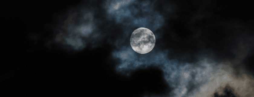 A full moon illuminates a cloudy night sky.