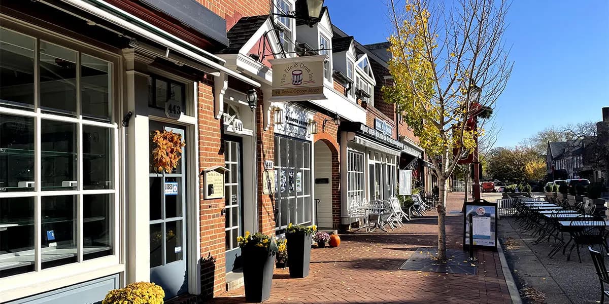 A quaint street lined with brick storefronts and outdoor seating under a clear blue sky.