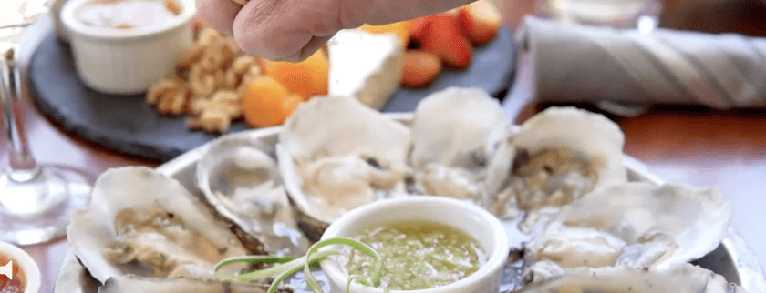 A hand sprinkles seasoning over a plate of raw oysters served with a dipping sauce. A hand sprinkles seasoning over a plate of raw oysters served with a dipping sauce.