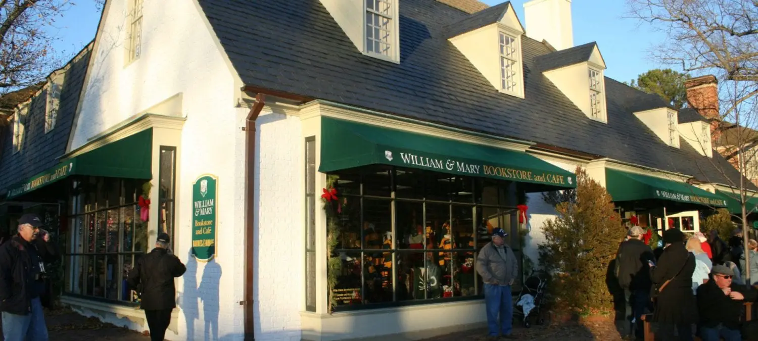 A bookstore and cafe adorned with holiday decorations, featuring large windows and a green awning, with people gathered outside. A bookstore and cafe adorned with holiday decorations, featuring large windows and a green awning, with people gathered outside.