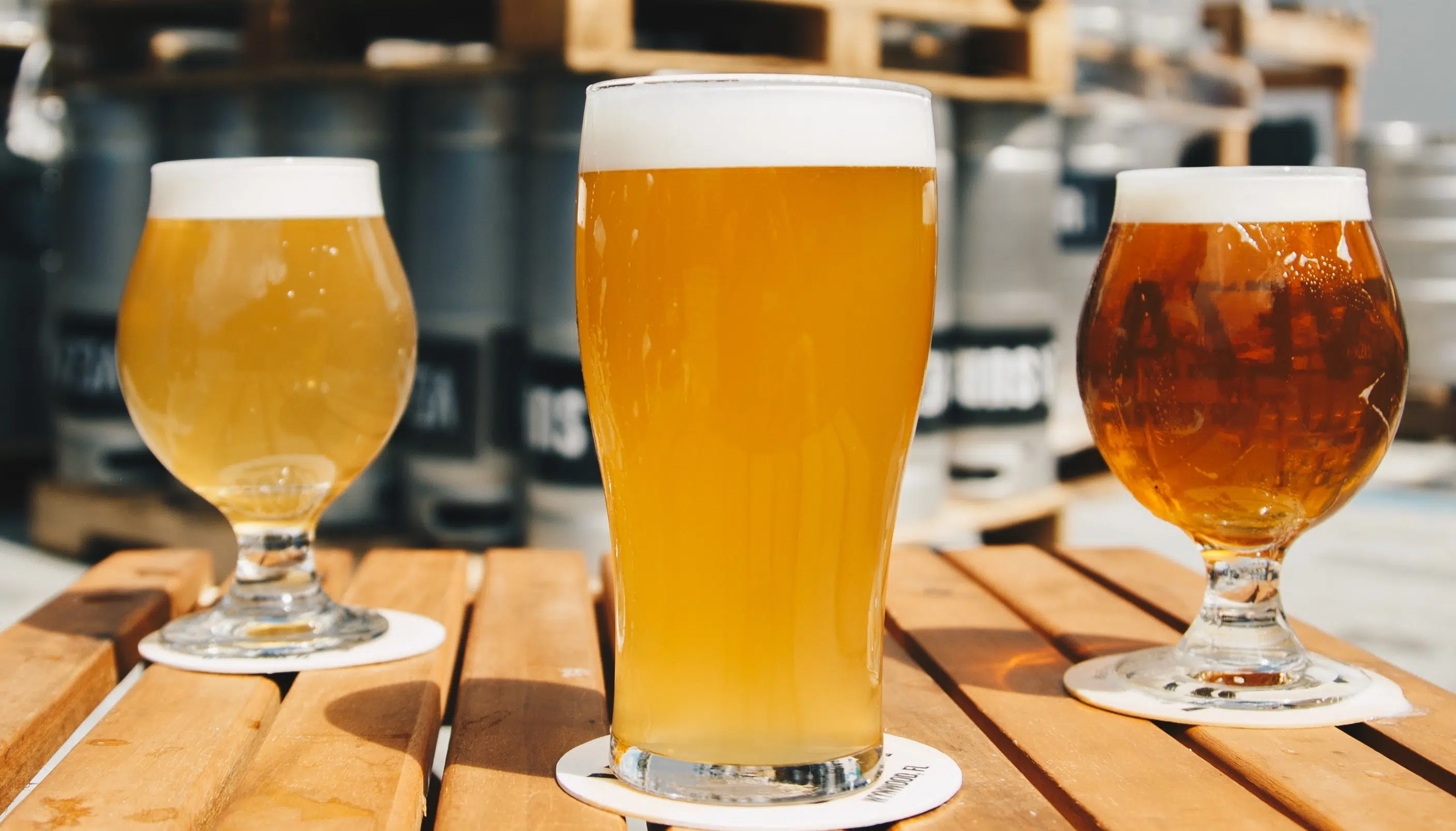 Three glasses of beer in various colors are displayed on a wooden table. Three glasses of beer in various colors are displayed on a wooden table.