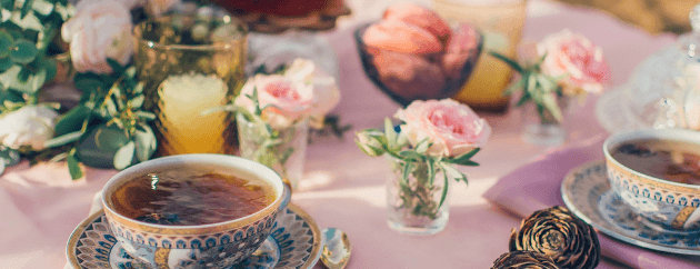 A beautifully set table with tea cups, floral arrangements, and sweet treats.