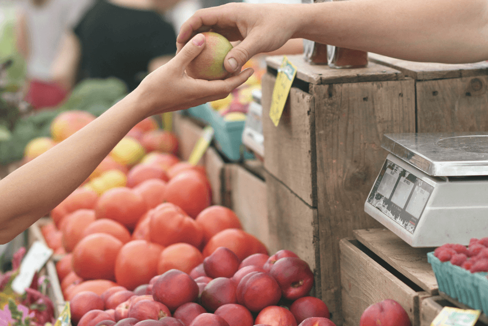 Man handing woman red apple at farmers market