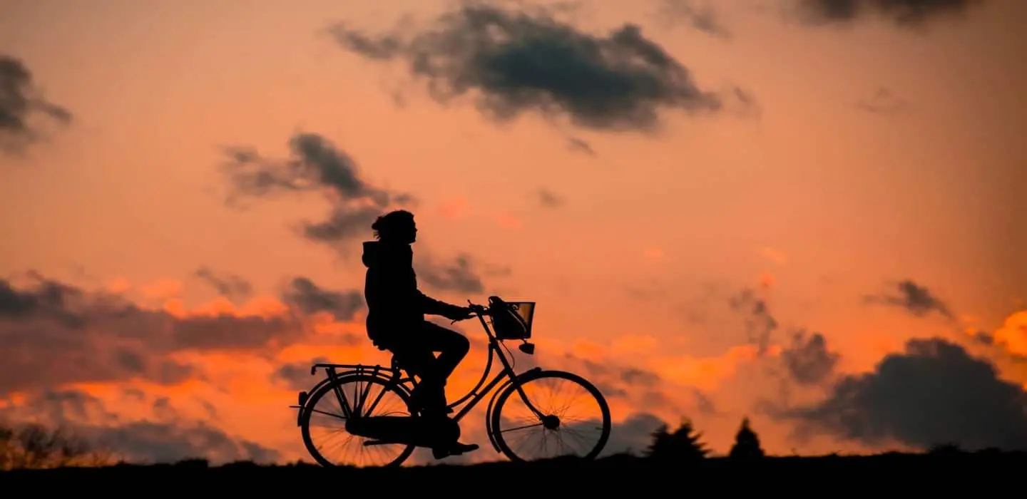 A silhouette of a person riding a bicycle against a colorful sunset.