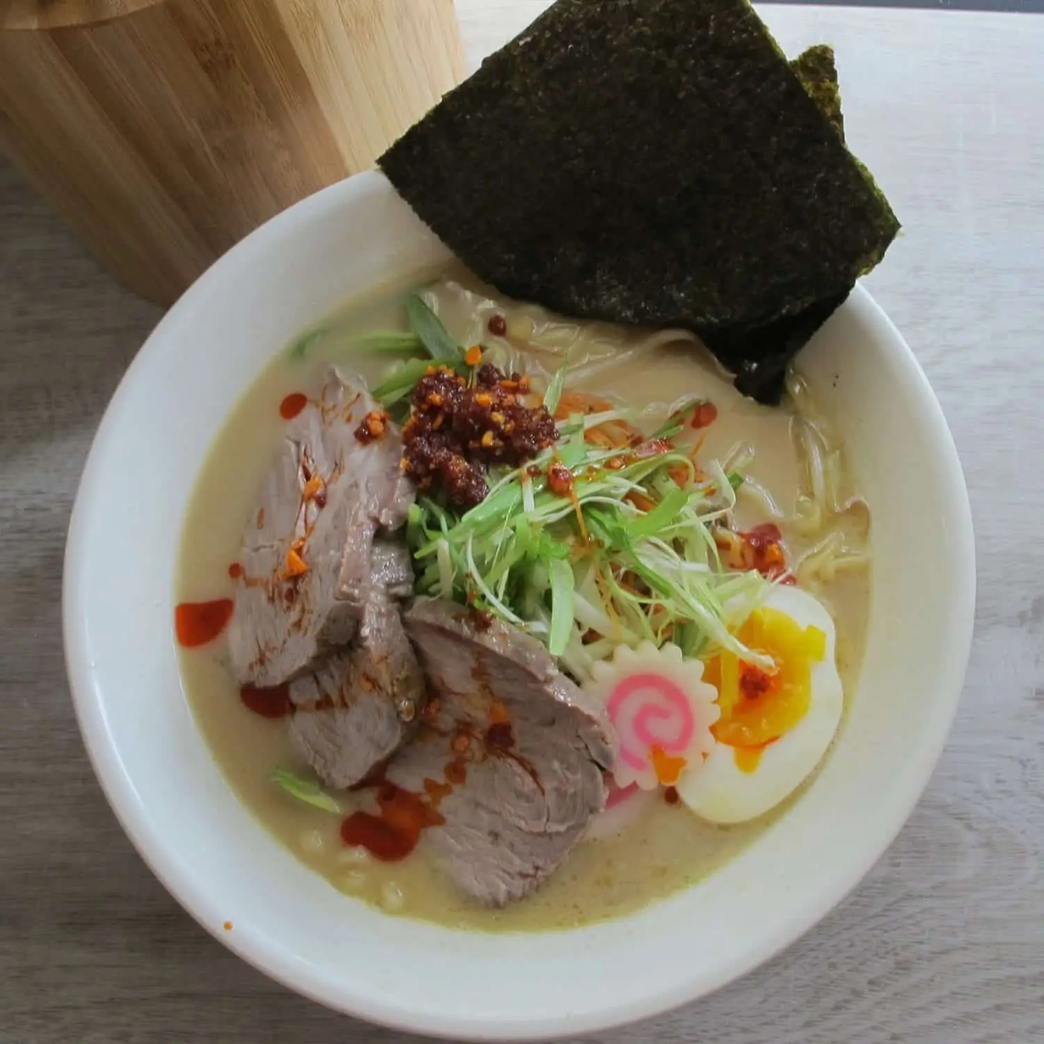 A bowl of ramen topped with sliced beef, green onions, a boiled egg, and a piece of seaweed.